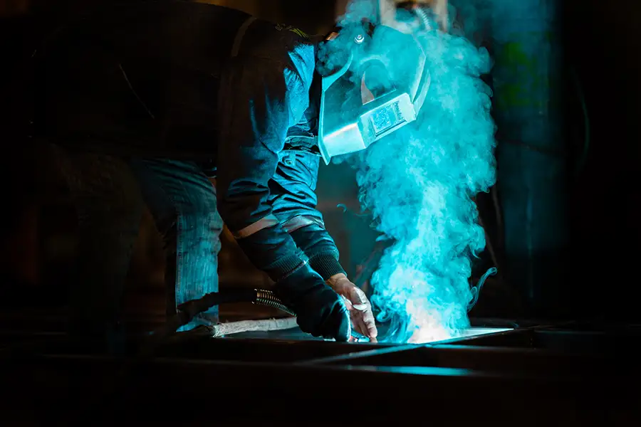 Manual welder in mask, with visible weld fume. Personal particulate monitoring allows measurement of exposure levels for individual workers.