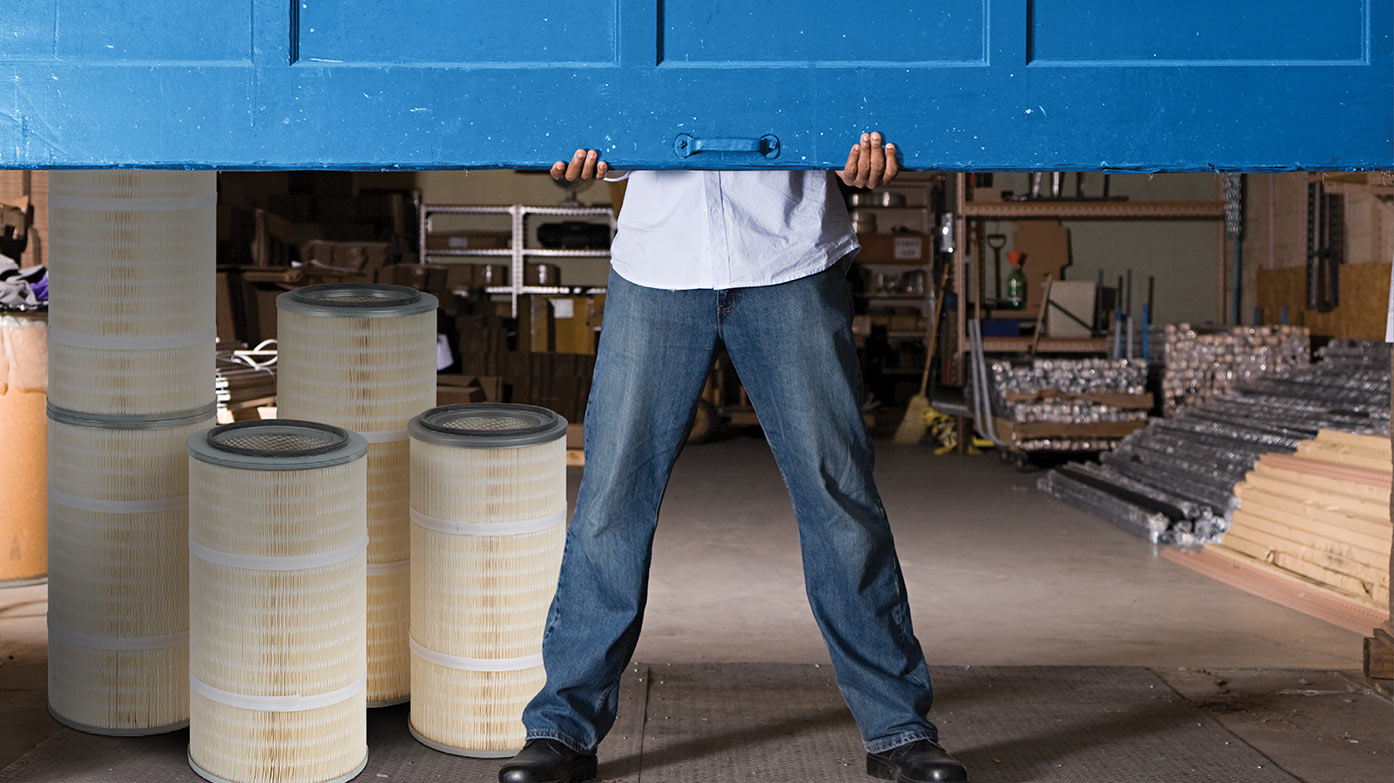 Man holding a garage door halfway down with supplies in the background.
