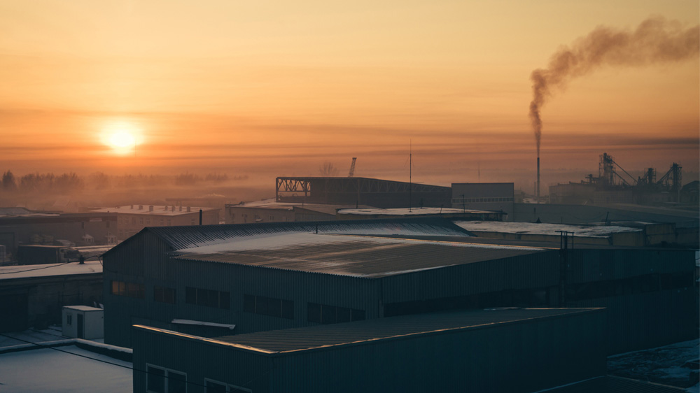 Bird's-eye view during sunset of factory with smoke coming out during the winter.