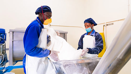 Two men in a factory pouring bulk powder into machine.