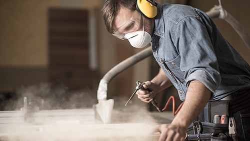 Masked man doing woodworking with with fine dust particles in the air.