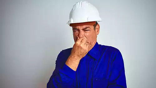 Man in blue shirt and white hat pinching his nose and making a face due to a smell.
