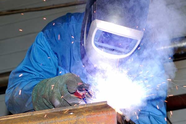 Industrial welder surrounded by fumes in a facility that needs weld fume extraction