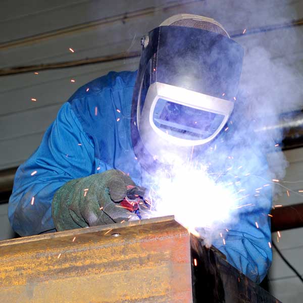 Industrial welder surrounded by fumes in a facility that needs weld fume extraction