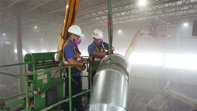 Green crane loading big blue RoboVent containers, preparing to install industrial dust collection system