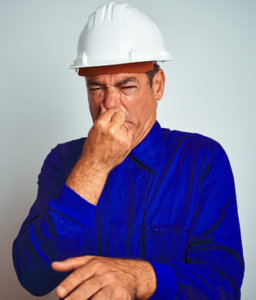 Man in blue shirt and white hat pinching his nose and making a face due to a smell.