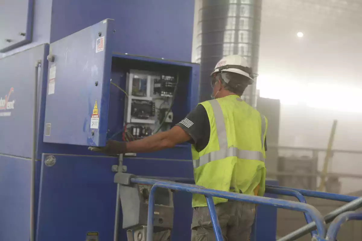 Industrial facility manager reviewing a dust collector control panel inside a manufacturing plant.