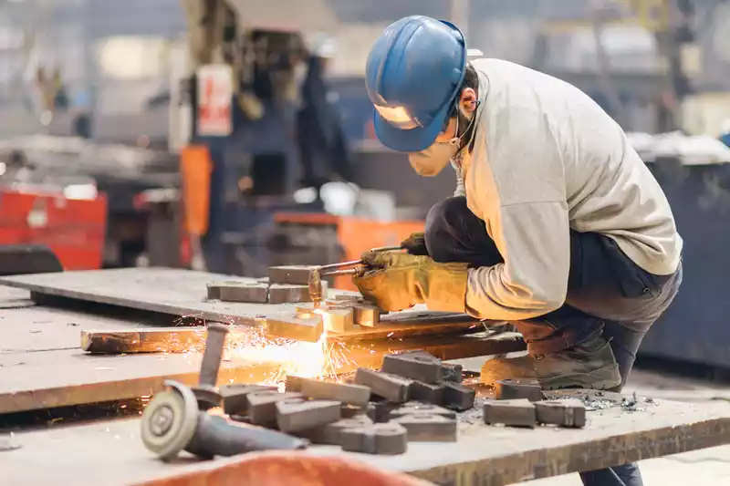 A man using an oxy-fuel torch to cut shapes out of a thick steel plate, with visible sparks.