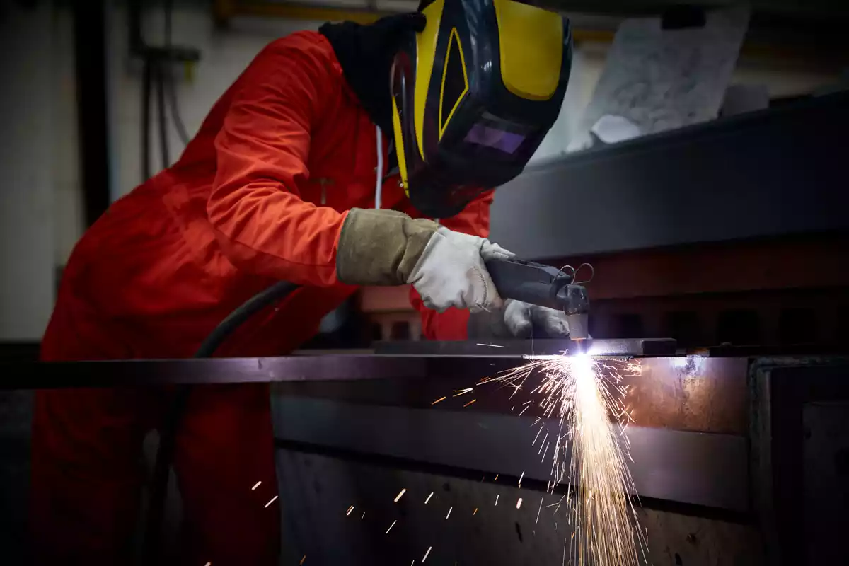 A person performing manual plasma cutting on a metal plate, with bright sparks flying from the cutting torch.
