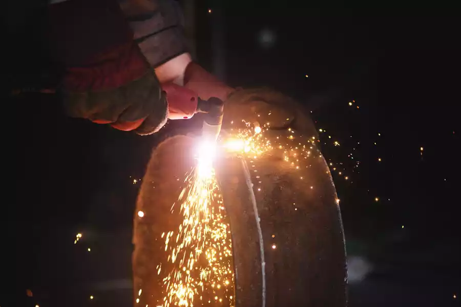 Close-up of a person using a handheld plasma cutter to cut through a sheet of metal, producing a bright arc and sparks.