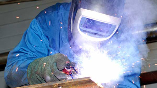 Close up of a welder wearing protective gear and manually welding a steel beam.