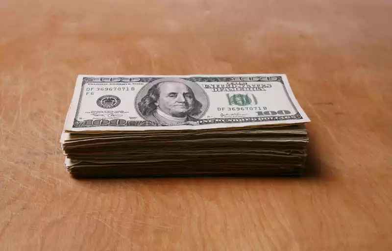 A stack of $100 bills on a brown tabletop.