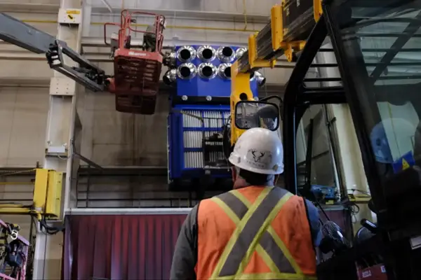 Worker in safety gear oversees the installation of a large RoboVent dust collector using a forklift and lift equipment.